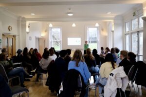 A large group of prospective students seated facing a presenter at the front of the room during a talk at a Diploma Open Day.