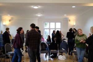 A diverse group of attendees mingling and laughing together during a break at a Diploma Open Day, in a spacious, light-filled room.