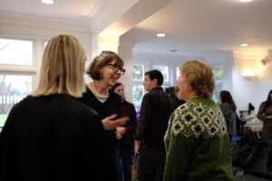 Attendees mingling and chatting at a Diploma Open Day, with a woman in glasses and a black jumper smiling warmly mid-conversation in a bright, modern room.