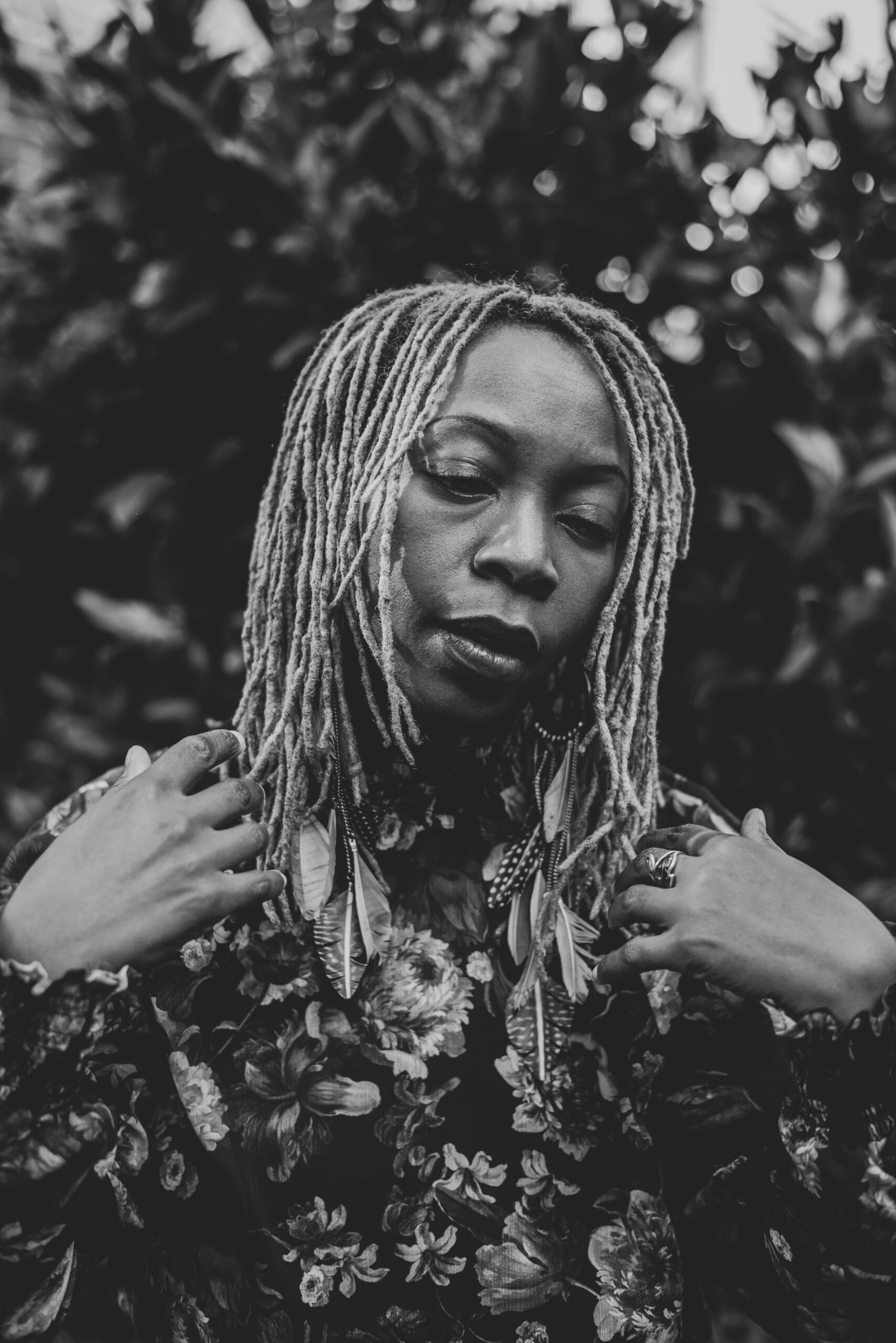 A black and white portrait of a woman with locs, eyes closed, set against a backdrop of leaves.